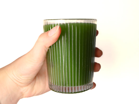 Main tenant un verre strié de matcha pur vert intense sur fond blanc