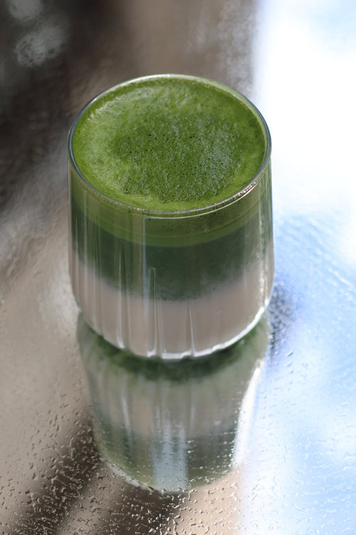 Matcha latte Supramatcha dans un verre, reflété sur une surface humide